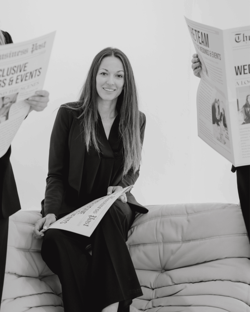Wedding planner sitting relaxed on a sofa holding a stylized wedding newspaper