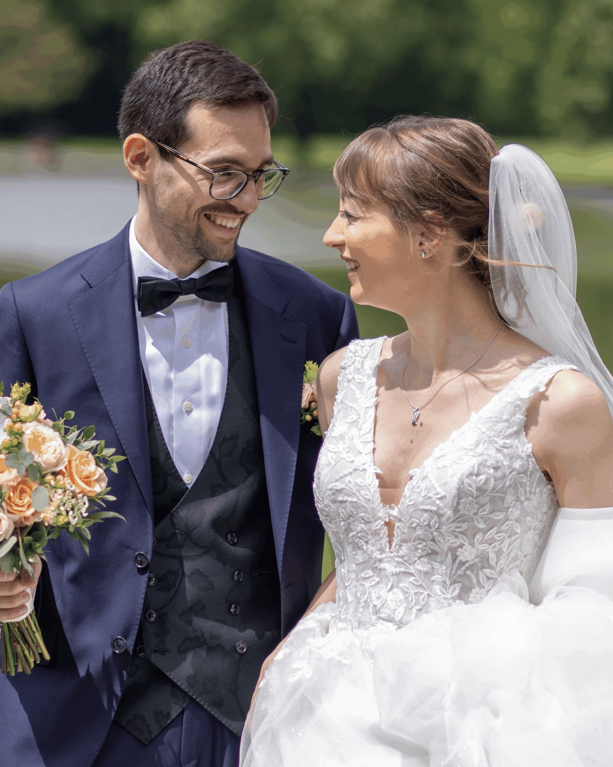Smiling bride and groom in elegant wedding attire gaze lovingly at each other, outdoor portrait