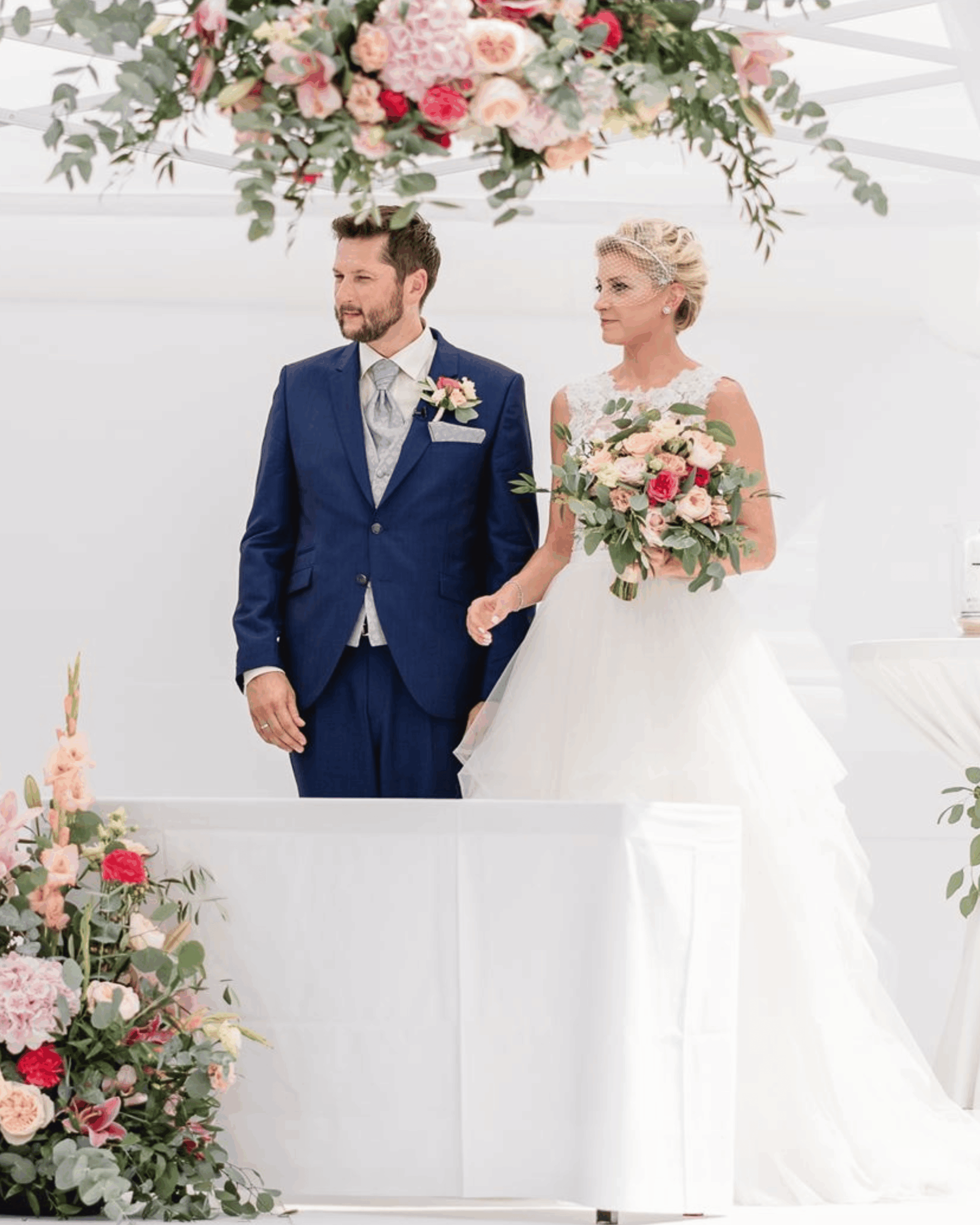 Bride and groom standing side by side during the ceremony, holding bouquets and looking forward