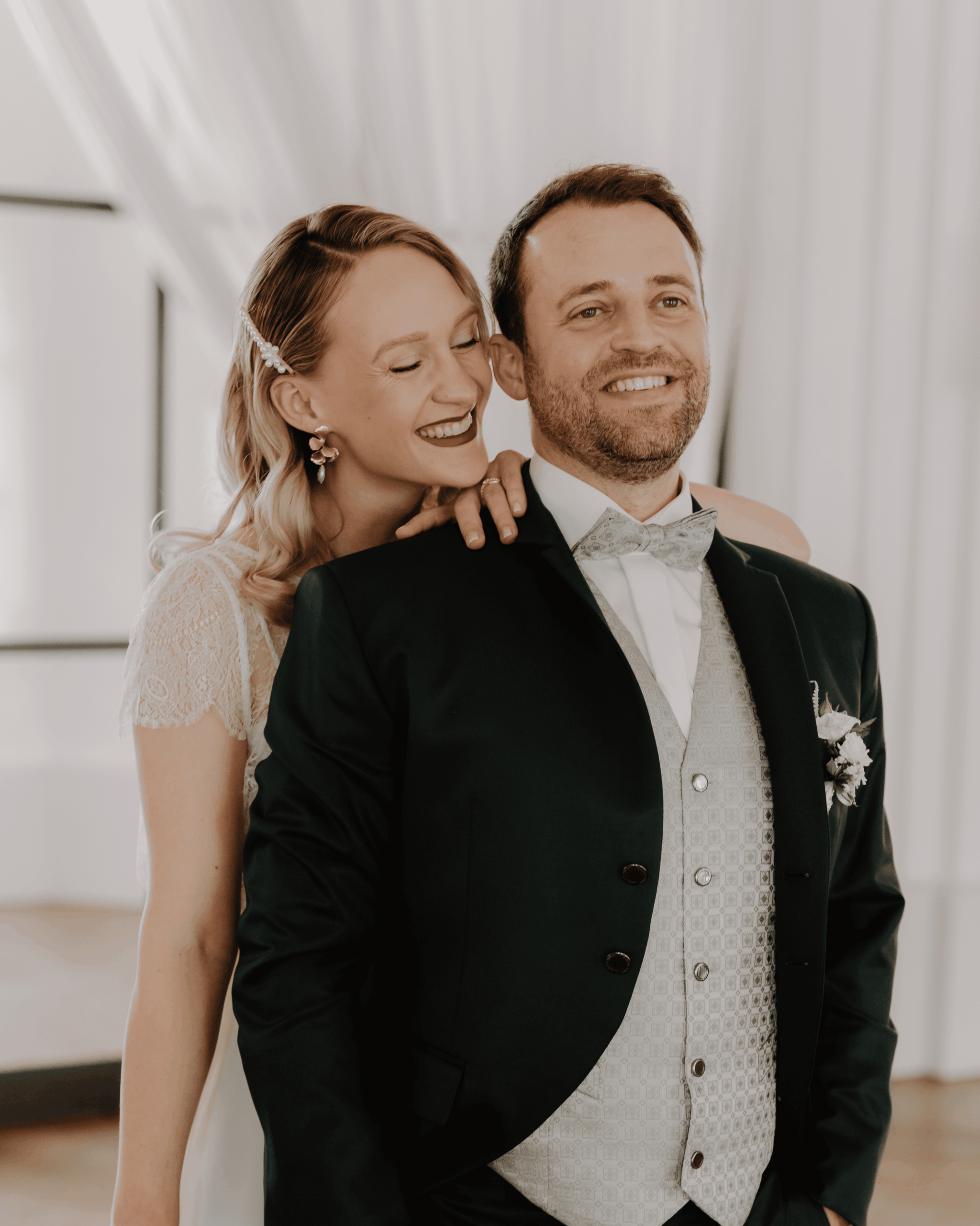 Bride leaning against the groom with a smile, emotional wedding portrait in a bright interior