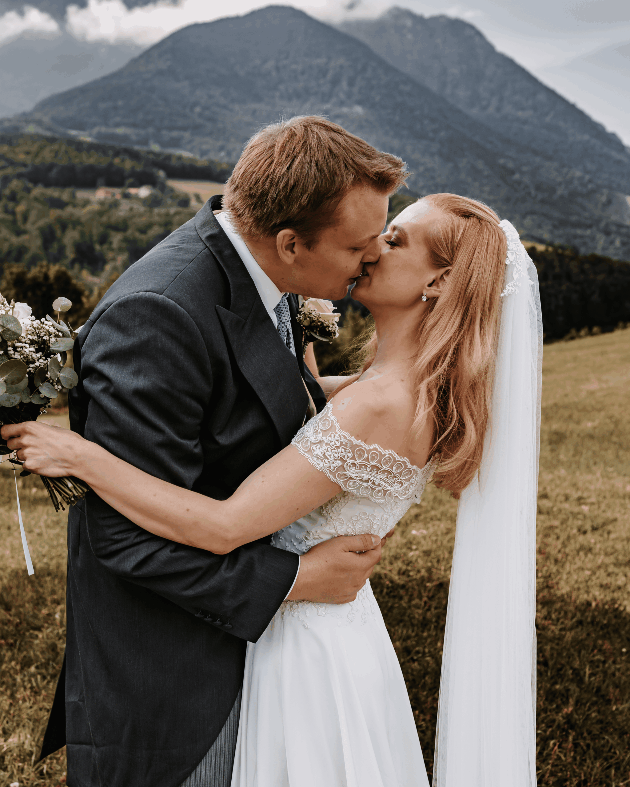 Bridal couple kissing in front of a mountain landscape, romantic wedding portrait in nature